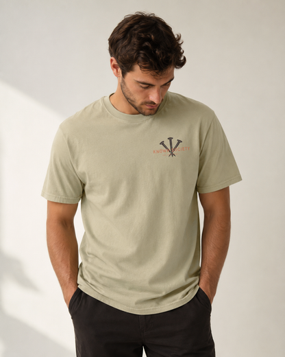 Man wearing the khaki Known Society men’s Christian T-shirt with three-nail chest design and Isaiah 43:1.