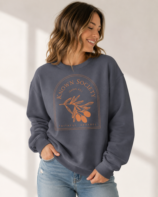 Joyful woman wearing the denim blue Known Society Christian sweatshirt with Isaiah 43:1 olive branch design