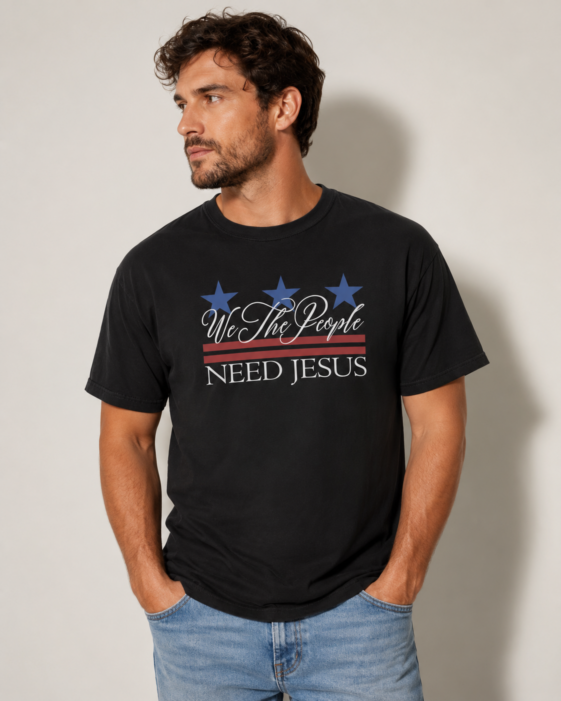 Male model wearing a black We the People Need Jesus Christian T-shirt against a neutral off-white studio background.