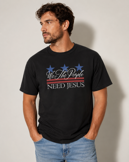Male model wearing a black We the People Need Jesus Christian T-shirt against a neutral off-white studio background.