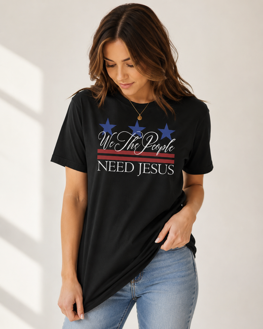 Woman looking down while wearing a black We the People Need Jesus patriotic Christian T-shirt.