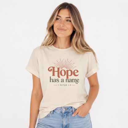 Woman wearing an ivory Hope Has a Name Christian T-shirt with 1 Peter 1:3 graphic and light-wash jeans